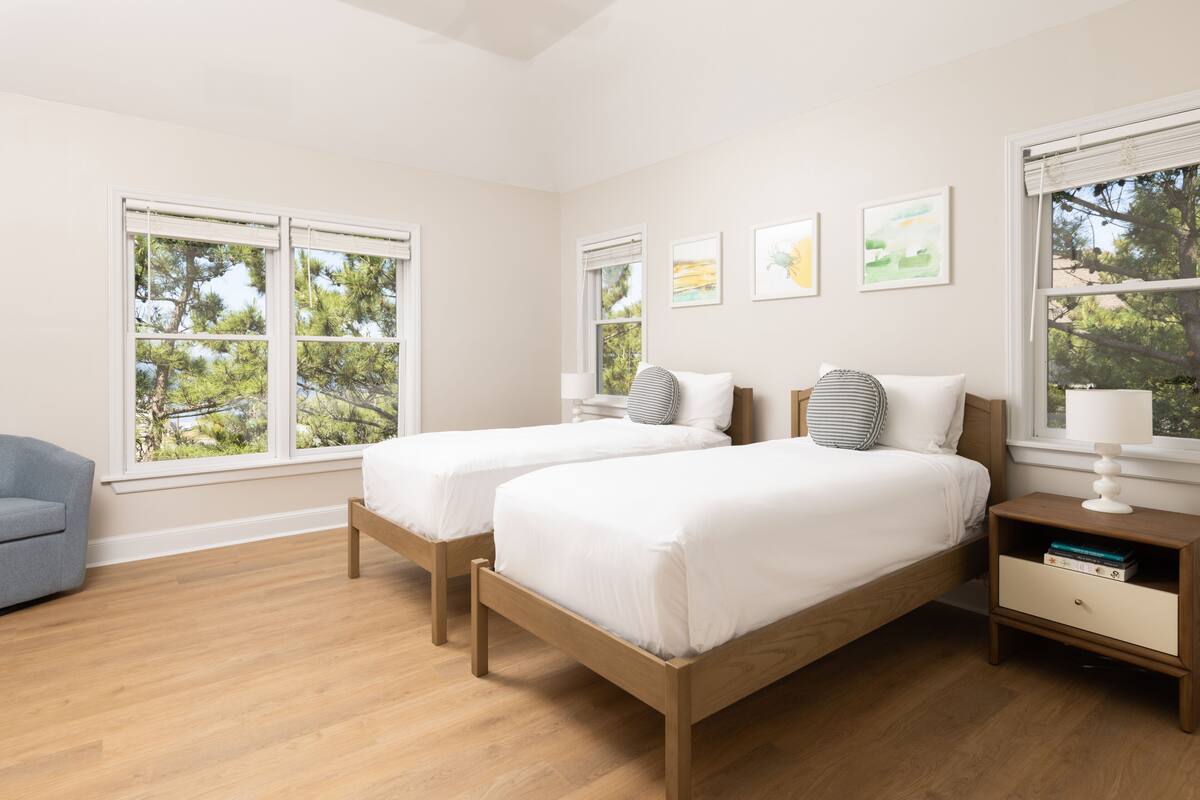 Un dormitorio con dos camas, una mesita de noche, una lámpara y una silla.