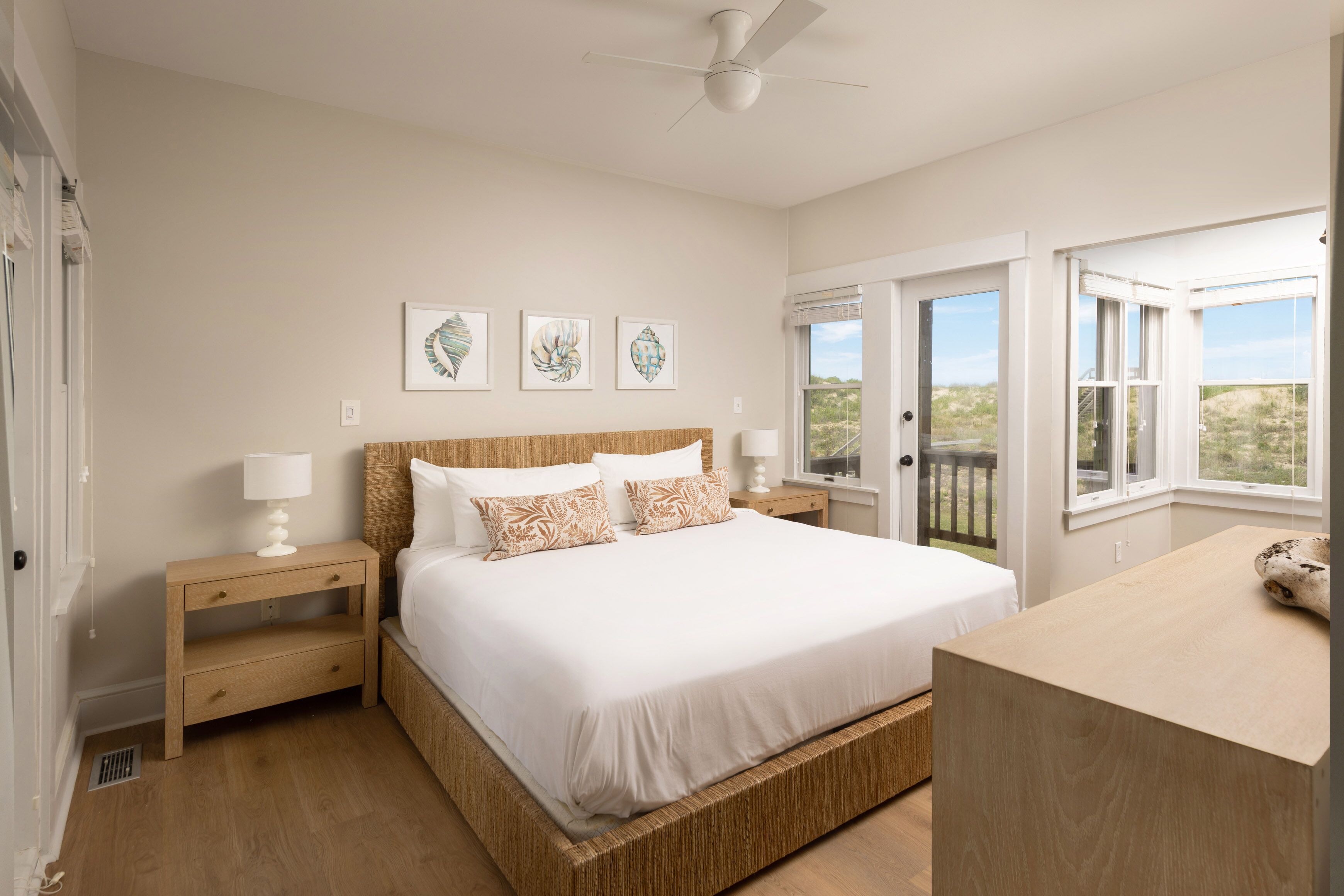 A bedroom with a large bed, bedside tables, a ceiling fan, and a view through a window.