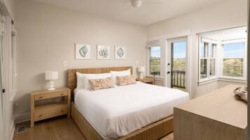 A bedroom with a large bed, bedside tables, a ceiling fan, and a view through a window.