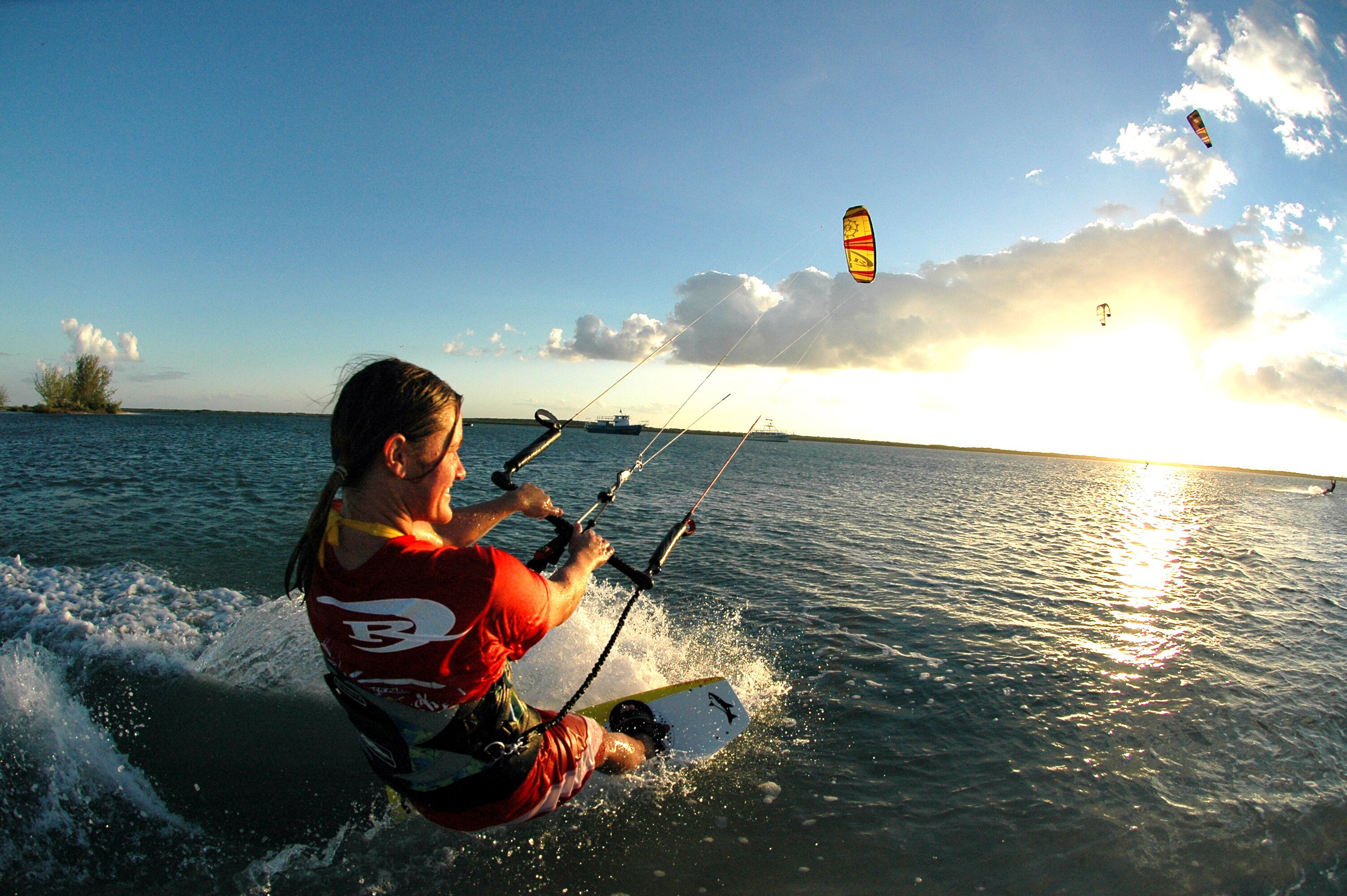 A person windsurfing on a body of water with a clear sky and a sunset in the background.