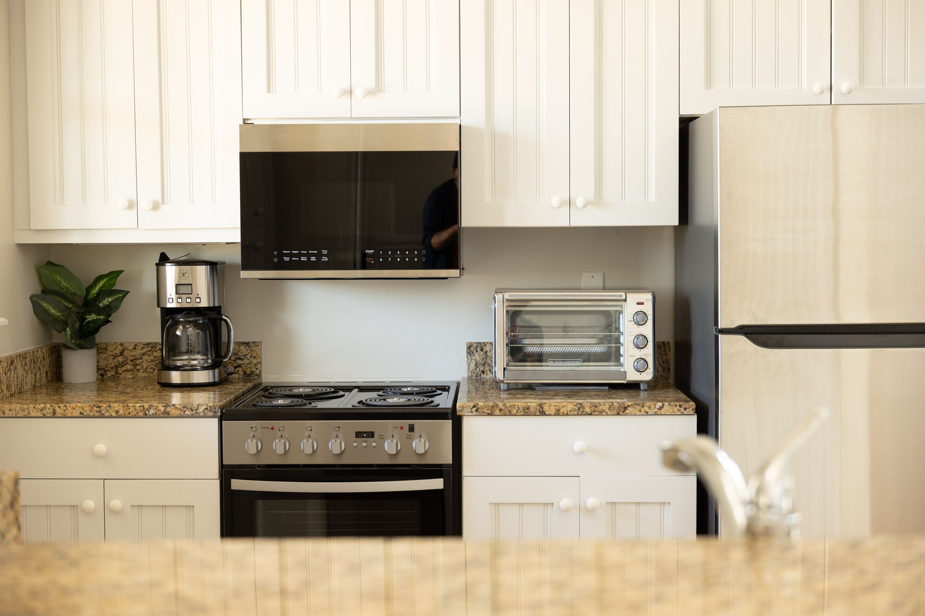 A kitchen with white cabinets, a stainless steel stove, a microwave, a toaster, and a refrigerator.