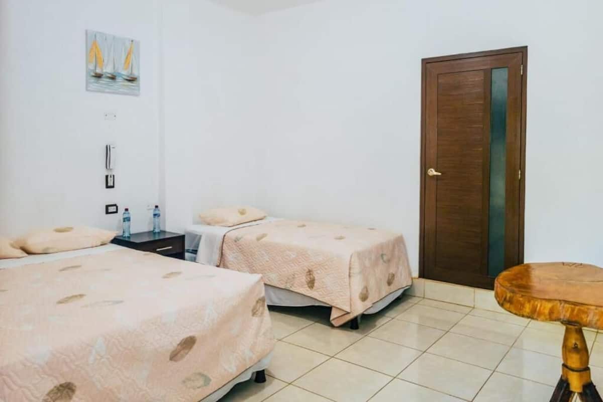 Habitación de hotel con dos camas, una puerta de madera, una mesita y un cuadro en la pared.