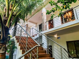 Interior com vários níveis, escada de madeira, guarda-corpos metálicos e plantas.