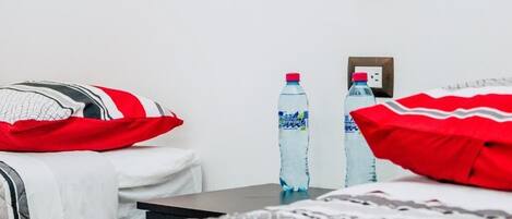 Habitación de hotel con una cama, almohadas, una mesa y dos botellas de agua.