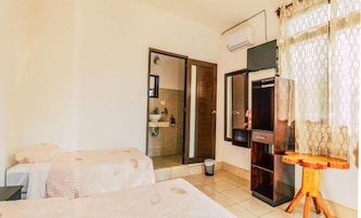 Quarto de hotel com duas camas, banheiro com chuveiro e uma mesinha de cabeceira de madeira.