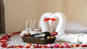 Un letto con un'accogliente disposizione di asciugamani a forma di cuore, una bottiglia di vino, due bicchieri e un cesto di petali di rosa.