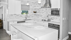 Una cocina moderna con armarios blancos, una isla grande con taburetes de bar, horno empotrado e iluminación colgante.