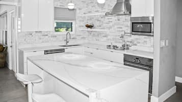 Una cocina moderna con armarios blancos, una isla grande con taburetes de bar, horno empotrado e iluminación colgante.