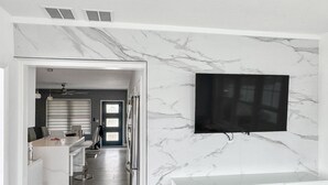 Una cocina moderna con salpicadero de mármol, horno empotrado y comedor con mesa y sillas blancas.