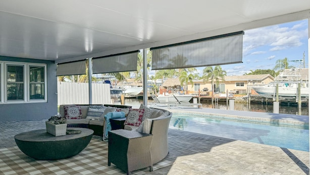 Un espacio de estar al aire libre cubierto, con piscina, suelo a cuadros y vistas a barcos y casas.