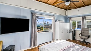Une chambre à coucher avec un lit, une télévision, un ventilateur de plafond et une fenêtre donnant sur la mer.