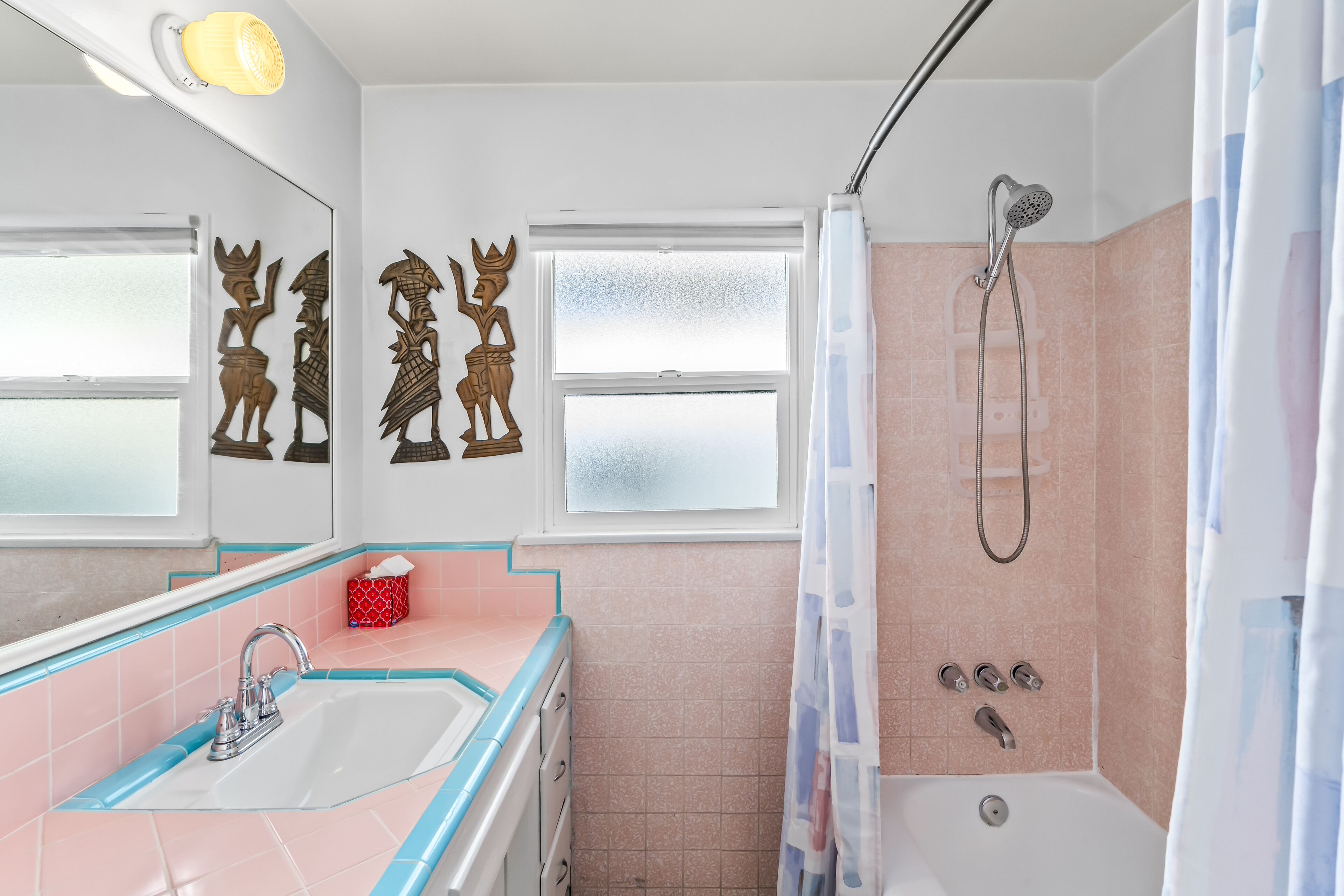 Une salle de bain équipée d’un lavabo, d’un miroir, d’une douche et d’œuvres d’art décoratives sur les murs.