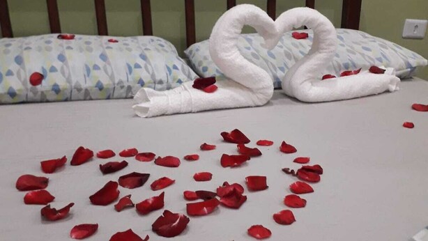 A bed with a heart-shaped arrangement of rose petals and two swan-shaped towels. - Aguas Quentes (Caraguatatuba)