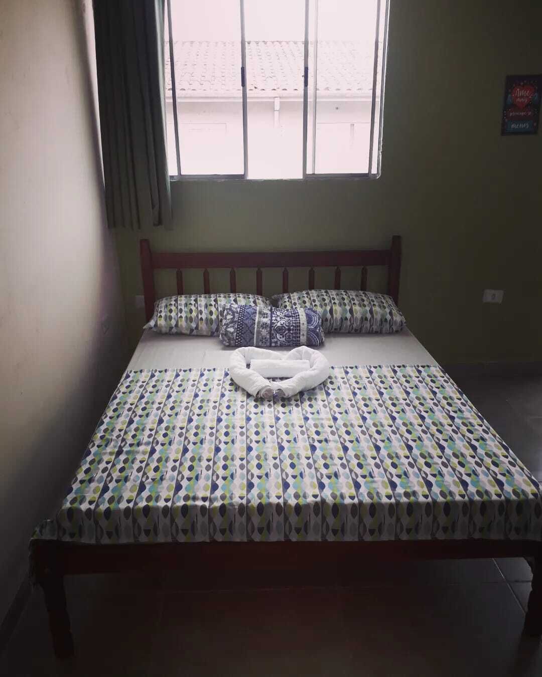 A single bed with a patterned bedspread, pillows, and a blanket folded at the foot of the bed.