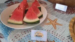 A table with a plate of watermelon slices, a basket of bread, a starfish decoration, and a small card. - Aguas Quentes (Caraguatatuba)