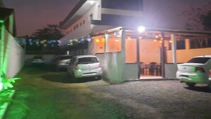 A building with a covered entrance and a parking area with several cars. - Aguas Quentes (Caraguatatuba)