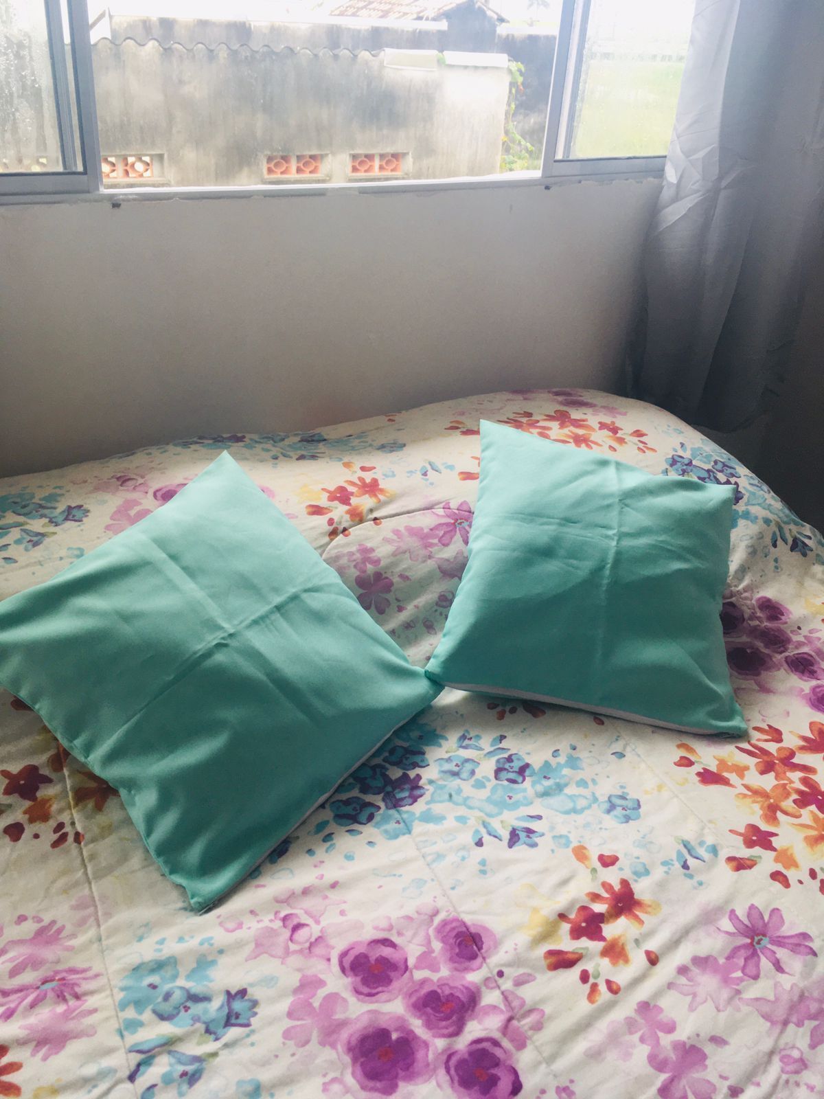 A bed with a floral bedspread and two teal pillows.