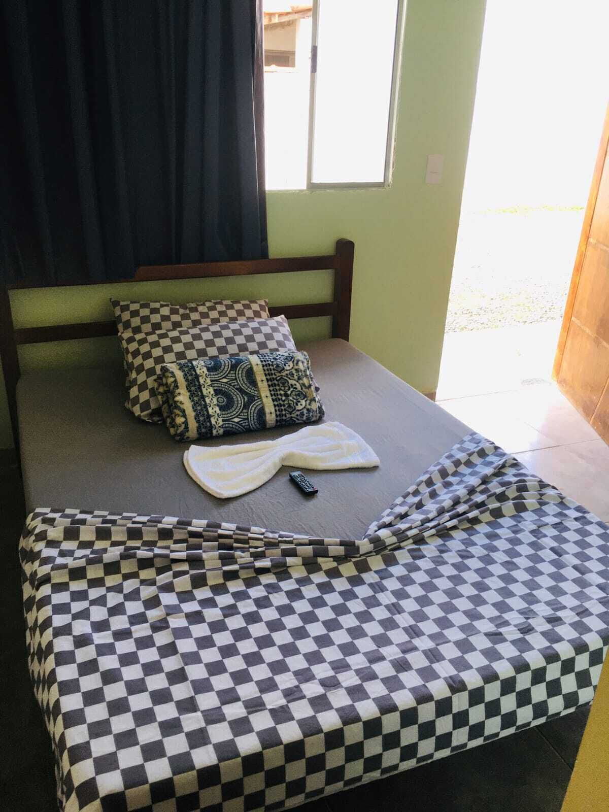 Una cama individual con una colcha a cuadros, un almohadón con diseño y un control remoto sobre la cama.