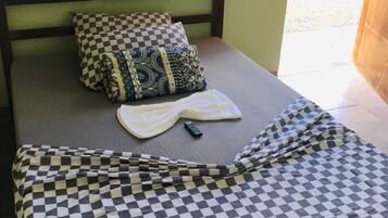 Una cama individual con una colcha a cuadros, un almohadón con diseño y un control remoto sobre la cama.