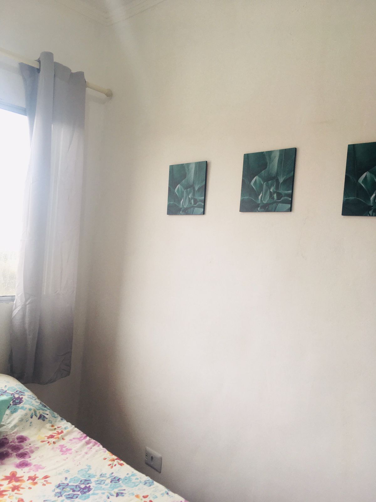 A room with a bed, a window with curtains, and three wall-mounted paintings.