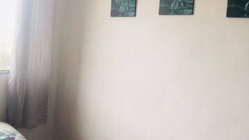 A room with a bed, a window with curtains, and three wall-mounted paintings.