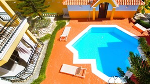 En swimmingpool med to liggestole, en mindre bygning med et tegltag og en trappe til en etage ovenover.
