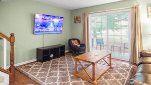 A living room with a wooden coffee table, a black entertainment unit, a blue chair, and a television mounted on the wall. - Townhouse in the Pines
 (Bloomington)