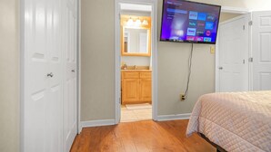 A bedroom with a bed, a TV mounted on the wall, and a bathroom visible through an open door. - Townhouse in the Pines
 (Bloomington)