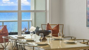 A dining area with a large window, a table set for four, and a view of the ocean. - Villas at Sunset Beach  (Panama City Beach)