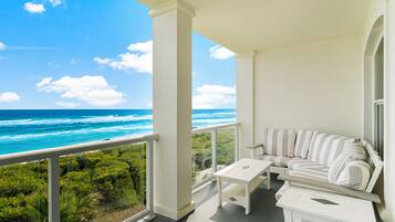 Un balcon avec un canapé et une table blancs, donnant sur une plage bordée par l’océan et une végétation luxuriante.