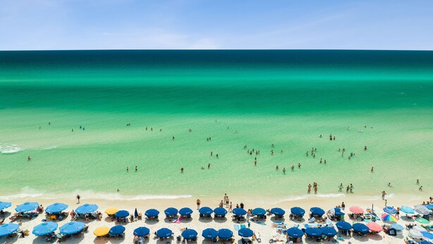 A beach with clear turquoise water, people swimming, and numerous beach umbrellas. - Villas at Sunset Beach  (Panama City Beach)