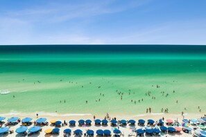 Une plage avec une eau turquoise et limpide, des gens qui se baignent et de nombreux parasols.