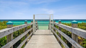 A wooden boardwalk leading to a gate with turquoise-topped posts, surrounded by greenery and overlooking a clear blue ocean. - Villas at Sunset Beach  (Panama City Beach)