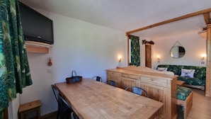 A cozy room with a wooden dining table, chairs, a sofa with a green leaf pattern, and a TV mounted on the wall. - 20m from ski slopes, 2nd floor, view ski slopes, balcony, 48m², La Plagne (La Plagne)