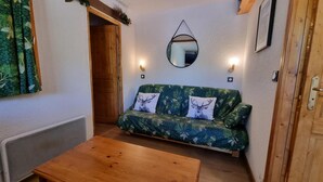 A cozy room with a green patterned sofa, two pillows with deer images, a wooden coffee table, a mirror on the wall, and a door with a wooden frame. - 20m from ski slopes, 2nd floor, view ski slopes, balcony, 48m², La Plagne (La Plagne)