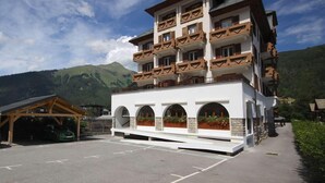 A multi-story hotel with balconies, a covered parking area, and a mountainous backdrop. - 2nd floor, balcony, parking, tv, ski locker, 45m², Morzine (Morzine)