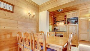 A wooden interior with a dining table and chairs, a kitchen area with wooden cabinets and appliances, and a framed picture on the wall. - 2nd floor, balcony, parking, tv, ski locker, 45m², Morzine (Morzine)