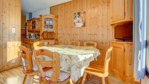 Ett rum med träpanel på väggarna, ett matbord, stolar, en tv och en köksdel.
