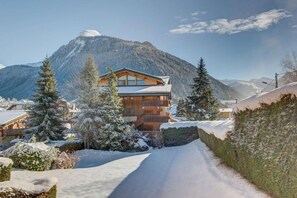 Un lodge in legno con un balcone, circondato da alberi innevati e montagne sullo sfondo.