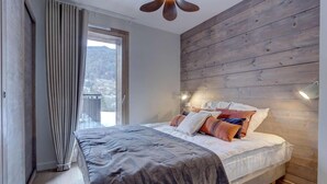 Een slaapkamer met een groot bed, houten wandpanelen, een raam met gordijnen en een plafondventilator.