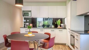 Een moderne keuken met witte kasten, een magnetron en een fornuis. Er staat een eettafel met rode stoelen en een potplant erop.