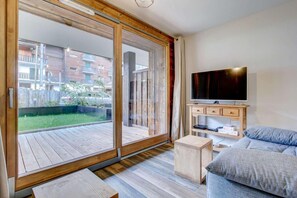 A modern living room with a large sliding glass door leading to a wooden deck, a flat-screen TV mounted on the wall, and a grey sofa. - Ground floor, terrace, parking, tv, 46m², Morzine (Morzine)