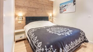 A bedroom with a wooden headboard, a patterned bedspread, and a wall-mounted picture of a ski slope.