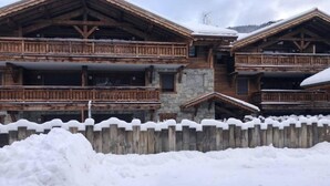 A wooden chalet with balconies and a stone facade, surrounded by snow.