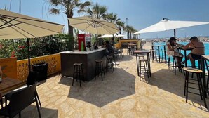 An outdoor bar area with tables and chairs, a counter, and umbrellas providing shade. - Duplex at Solemar Resort, Totally Renovated, Pools, Tennis, Basketball, Football (Jounieh)