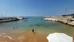 A beach with clear water, a rocky breakwater, and a few people swimming. - Duplex at Solemar Resort, Totally Renovated, Pools, Tennis, Basketball, Football (Jounieh)
