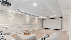 Una sala de cine en casa con una pantalla grande, asientos cómodos y un proyector de techo.