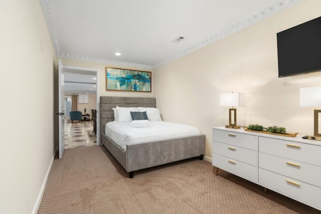 Une chambre à coucher avec un lit, une commode, un téléviseur et un tableau accroché au mur.