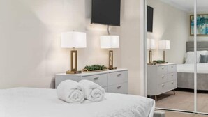 Habitación de hotel moderna con cama, mesita de noche con lámparas, armario y un espejo grande.