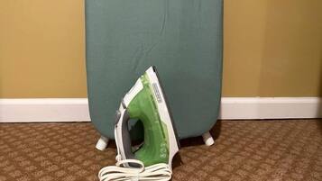 Una tabla de planchar verde con un cable blanco enrollado sobre una alfombra estampada.